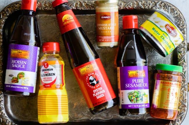 bottles of hoisin sauce, aji mirin, oyster sauce, hot mustard, sesame oil, water chestnuts, and chili garlic sauce on a tray