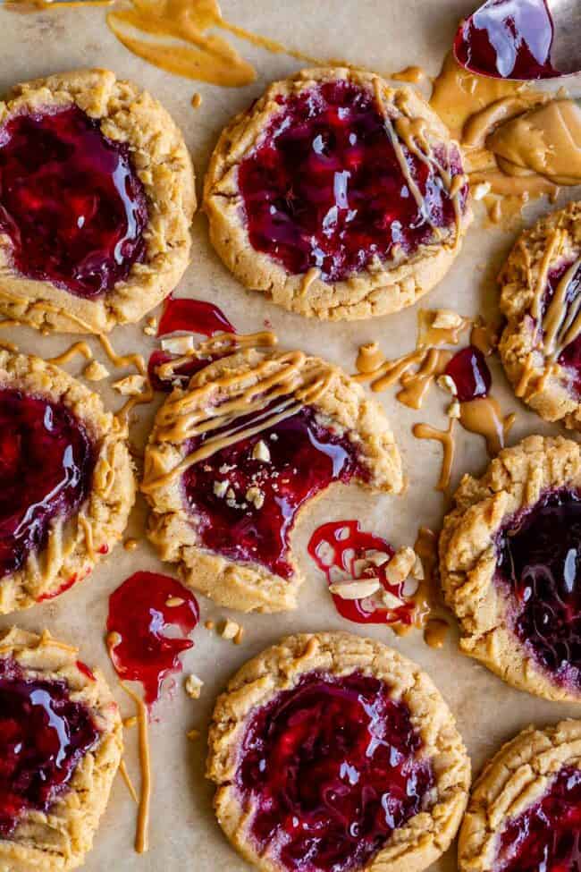 pb and j cookies on parchment paper with jam, peanut butter, chopped nuts garnish with