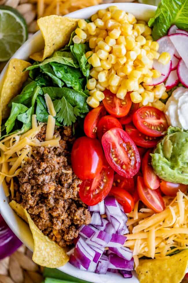 taco salad with meat, cheese, chips, and veggies in a white bowl.