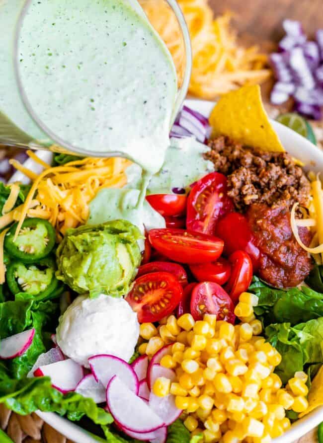 pouring creamy cilantro lime dressing on a bowl of taco salad.