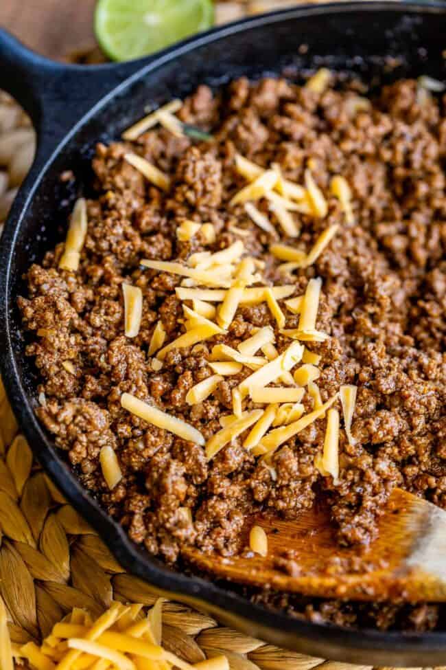 a cast iron pan full of taco meat, sprinkled with cheddar cheese