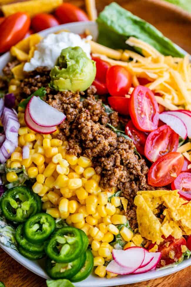 a bowl of taco salad with meat, corn, tomatoes, chips, guacamole, radishes, onions, and more.