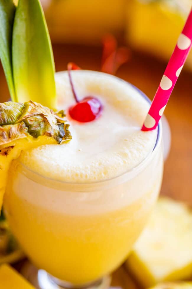 frothy virgin pina colada in a goblet with a polka dot straw, pineapple wedge, and maraschino cherry. 