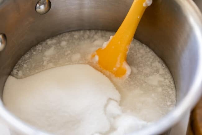 sugar, coconut milk, and salt in a pot with a yellow spatula.