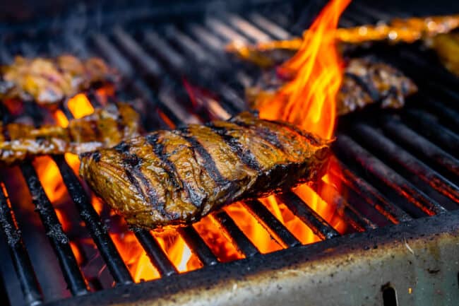 outside skirt steak on a grill with flames in the background.