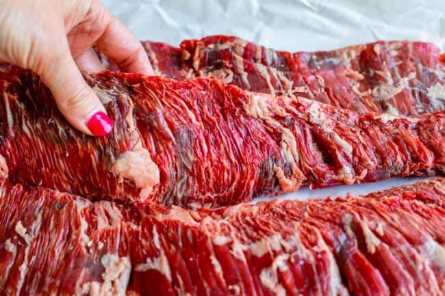 a long strip of raw outside skirt steak held with a hand.