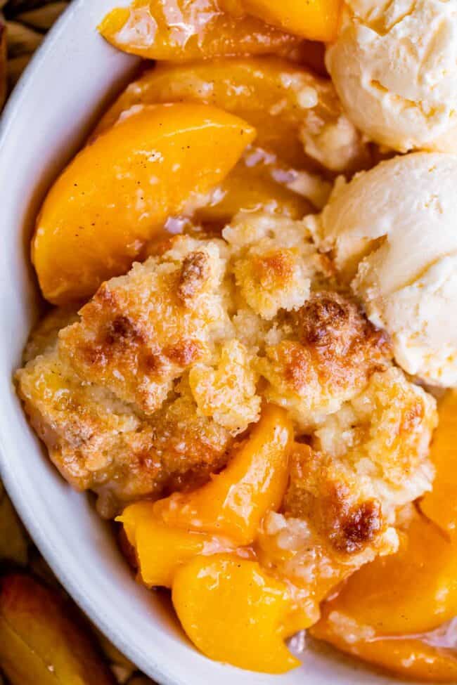overhead shot of peach cobbler in a white bowl with ice cream