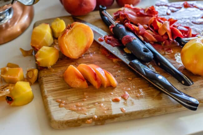 slicing peeled peaches on a cutting board.