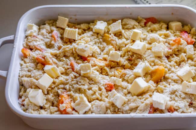 unbaked peach cobbler in a white casserole dish with cut butter on top.