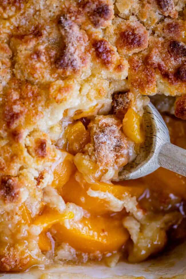 peach cobbler being scooped out of the pan with a spoon.