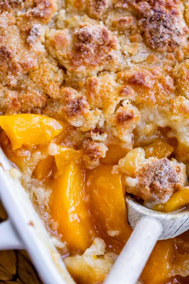 homemade peach cobbler in a white casserole dish with a wooden spoon