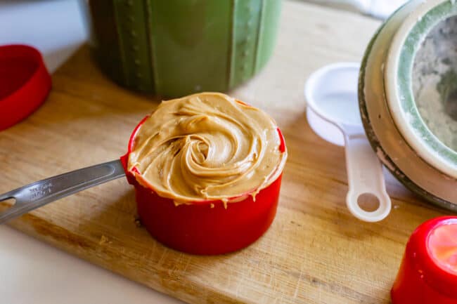 peanut butter in a red 1 cup measuring cup on a wooden cutting board.