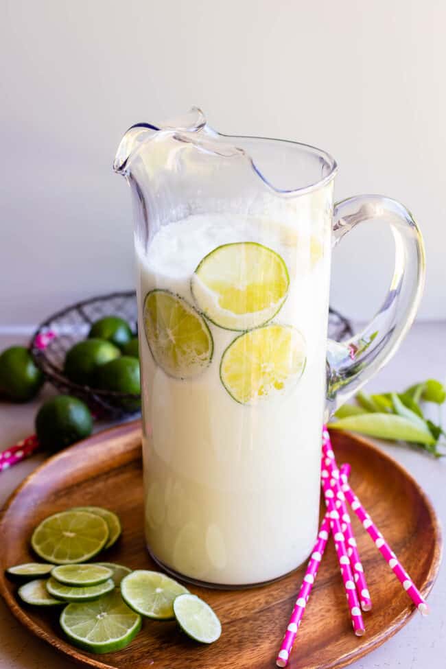 Brazilian lemonade recipe in a tall clear glass pitcher with pink polka dot straws and lime slices.