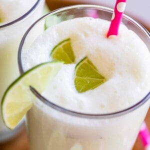 brazilian limeade in a glass with lime wedges and a pink straw