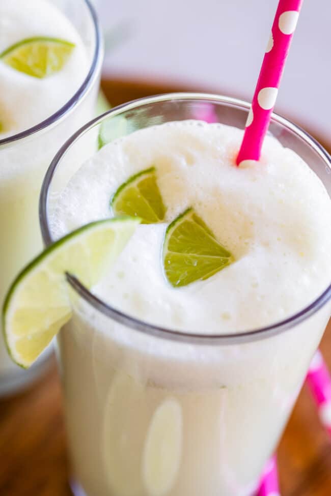 brazilian limeade in a glass with lime wedges and a pink straw.