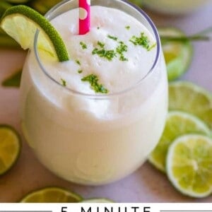 A creamy Brazilian limeade, also known as Brazilian lemonade, topped with lime zest and wedges, served in a glass with a pink polka-dot straw and surrounded by sliced limes. Text reads: 5-Minute Brazilian Limeade, Only 3 Ingredients, The Food Charlatan.