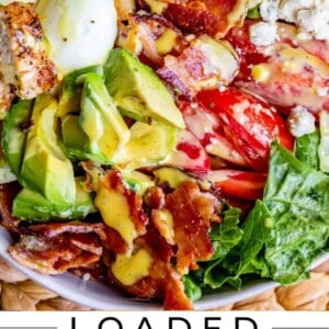 A bowl of Cobb salad with romaine lettuce, sliced avocado, hard-boiled eggs, bacon, chicken, tomatoes, feta cheese, and honey mustard dressing. Text: Loaded Cobb Salad with Honey Mustard—a classic cobb salad recipe favorite.