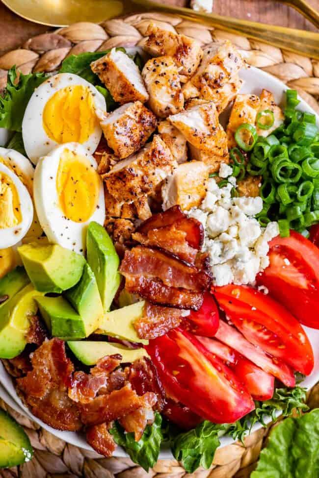 chicken cobb salad on a plate with tomatoes, boiled eggs, bacon, cheese.
