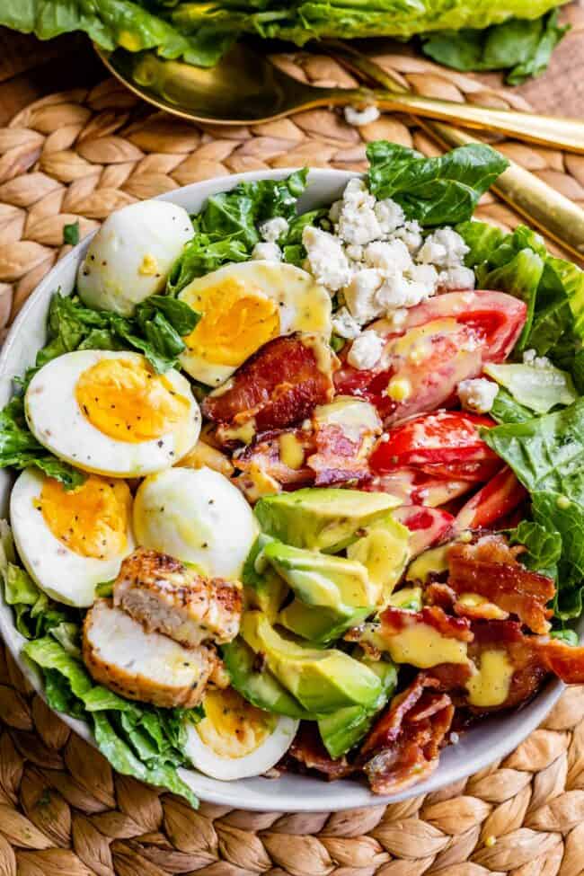 Cobb salad in a bowl with a gold serving spoon.