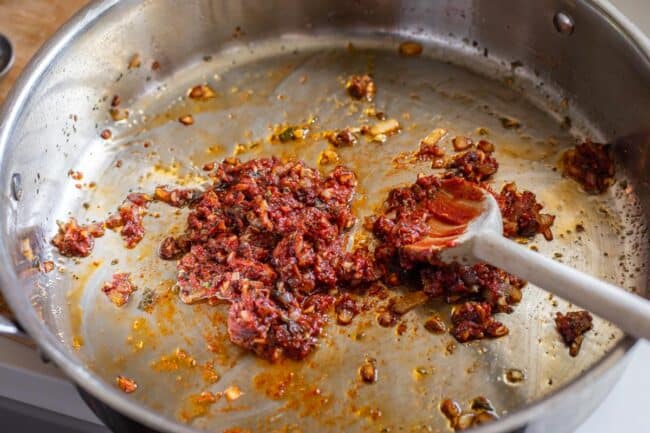 tomato paste, garlic, and spices being stirred in a pan with wooden spoon.