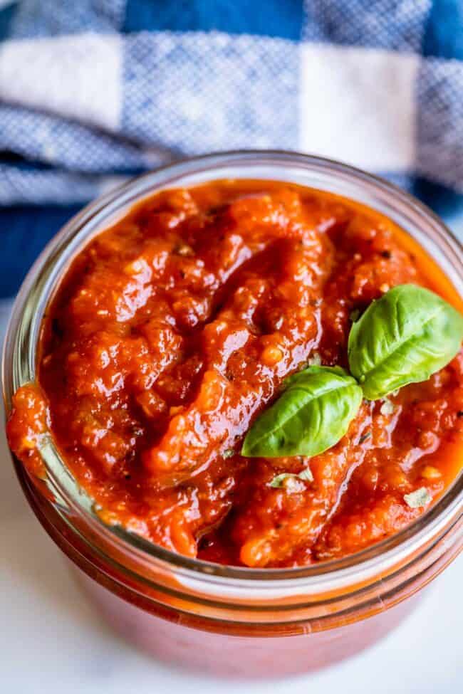 homemade pizza sauce in a jar with basil garnish.