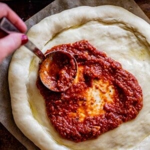 pizza sauce recipe being spread on a pizza dough with a ladle