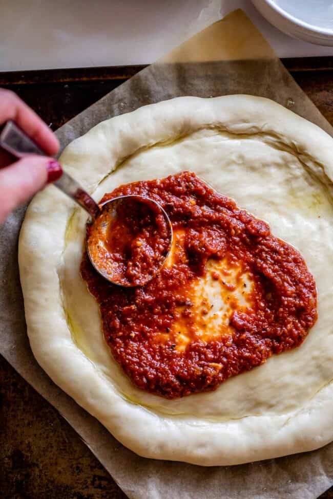 pizza sauce recipe being spread on a pizza dough with a ladle.