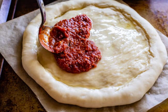 easy pizza sauce being spread on raw dough.