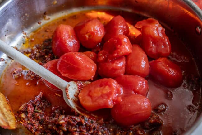 whole canned tomatoes being added to a pan to make best pizza sauce.