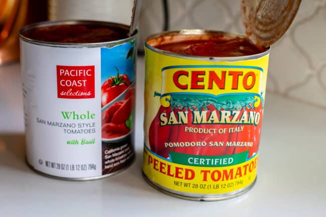 two different brands of canned whole tomatoes on a white countertop.