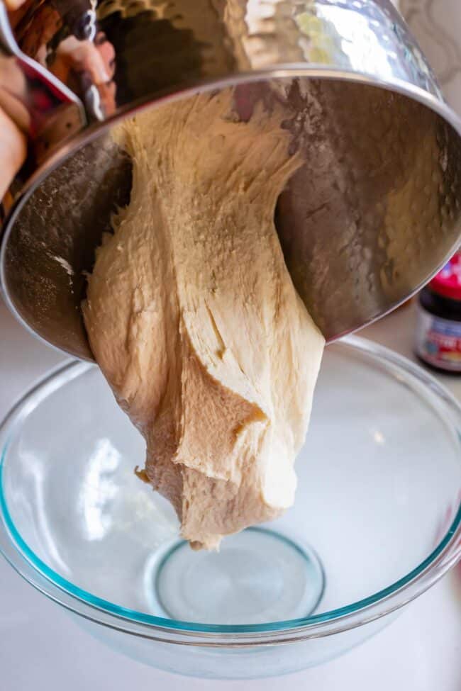 pouring a homemade pizza dough recipe from a stand mixer into a glass bowl.