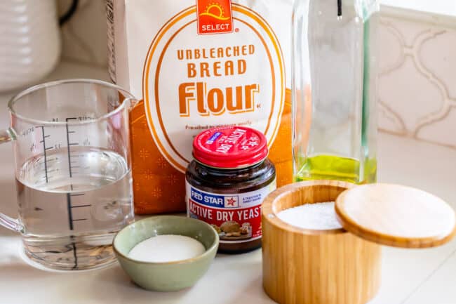 ingredients lined up on a counter for pizza dough: bread flour, yeast, salt, water.