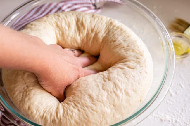 punching down pizza dough in a glass bowl.