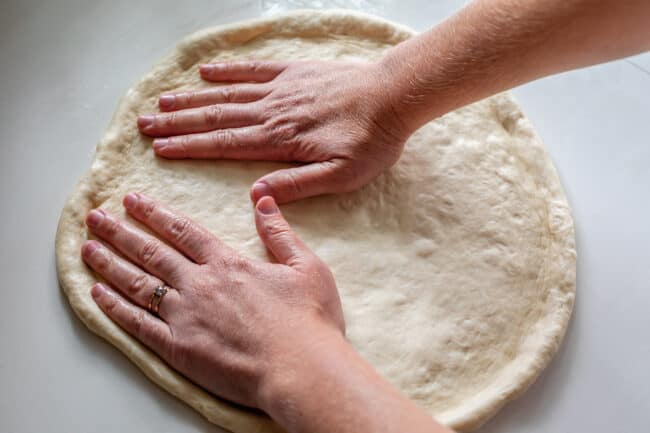 two hands spreading out and stretching pizza dough.