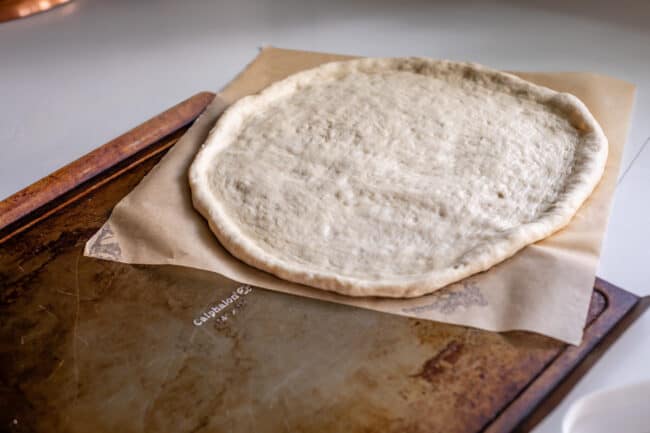 transferring raw pizza dough from counter onto flat baking sheet