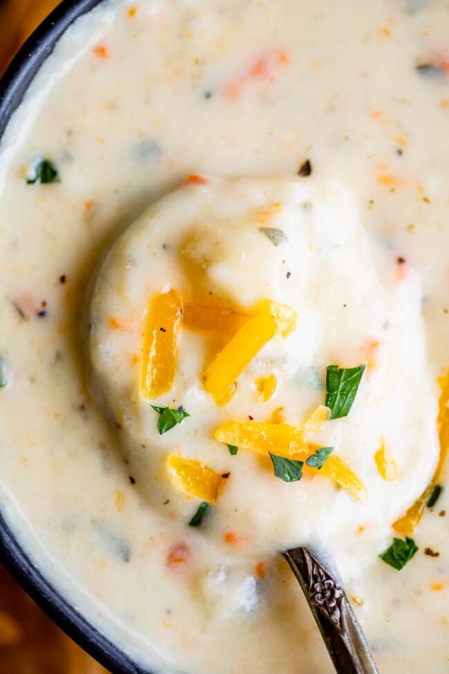 lifting cheesy potato soup from a bowl with a spoon.