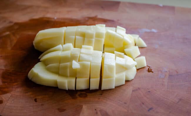 russet potato chopped into chunks on a cutting board.