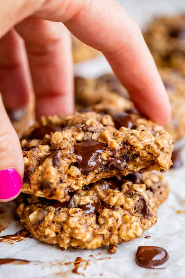 healthy chocolate chip cookies stacked with a bite taken, lifting with hand.