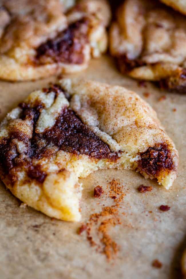 cinnamon roll cookies with bite taken out on a pan with cinnamon sprinkle