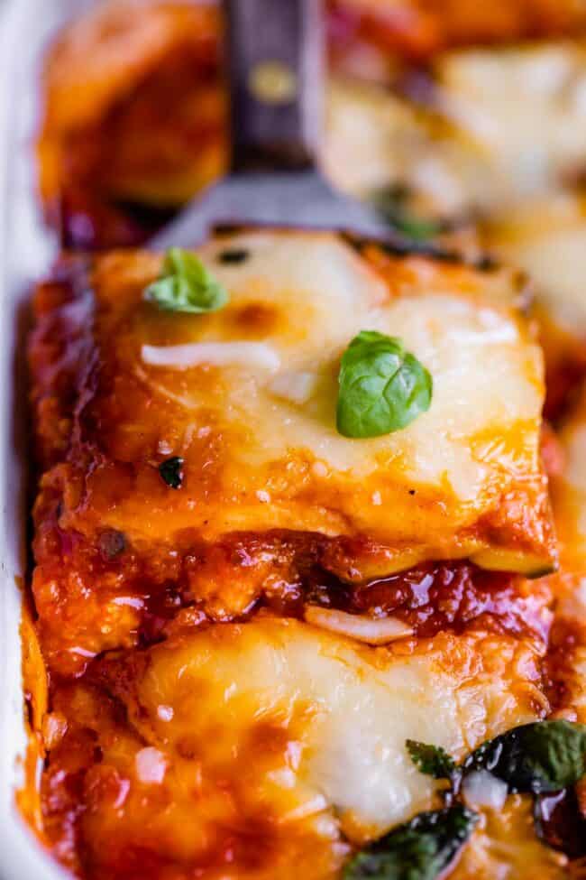 cheesy zucchini lasagna being lifted from the pan with a spatula, topped with basil