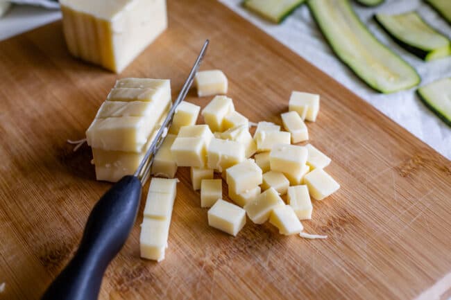 mozzarella cheese on a wooden cutting board because chopped into chunks with a knife