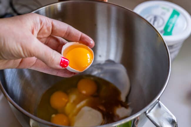 adding egg yolk to a stand mixer bowl with sour cream