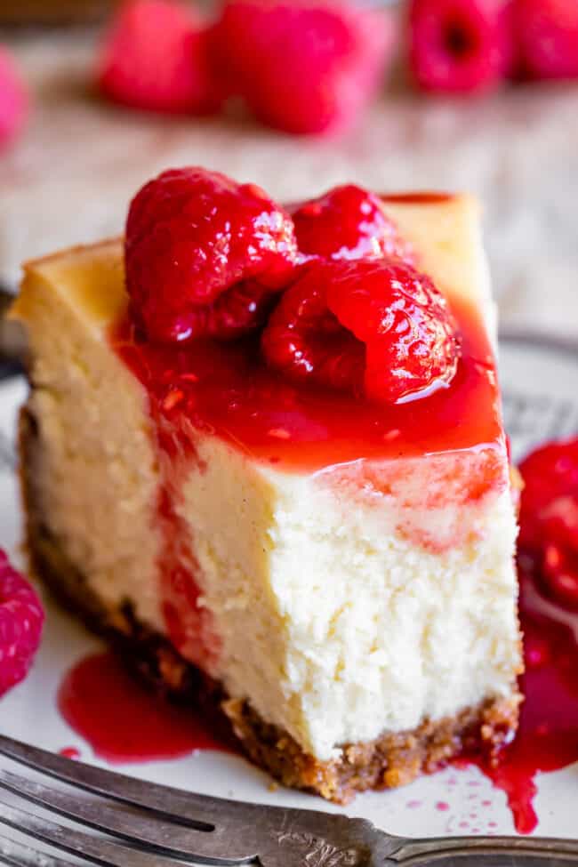 classic new york cheesecake with a bite taken out and raspberries