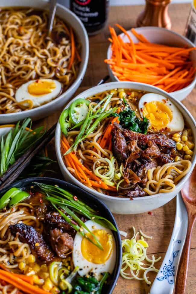 pork ramen broth in a bowl with carrots, pork, egg, and 2 other bowls of ramen nearby