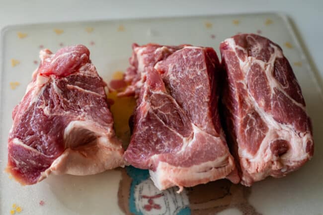 pork shoulder on a cutting board, chopped into 3