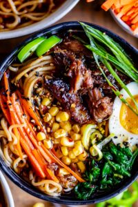 pork ramen in a black bowl with garnishes: carrots, egg, spinach, green onions