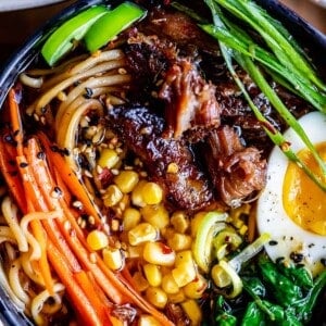 pork ramen in a black bowl with garnishes: carrots, egg, spinach, green onions
