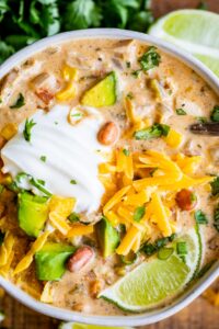 white chicken chili with sour cream and cheese garnish in a white bowl