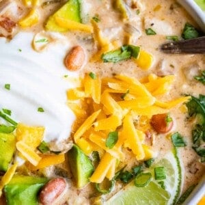 white bean chicken chili in a white bowl with lime and cheese garnish