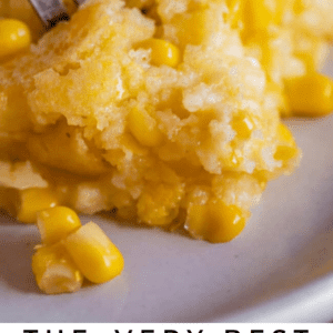 A close-up of a fork cutting into creamy corn casserole on a plate. The golden, moist dish shows visible kernels of corn. Text below reads: “The Very Best Creamed Corn Casserole – The Food Charlatan.”.